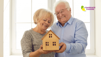 Un homme et une femme âgée tiennent à deux une maquette de maison en bois avec le sourire.
